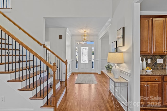 foyer entrance featuring crown molding, wood finished floors, stairs, and a decorative wall