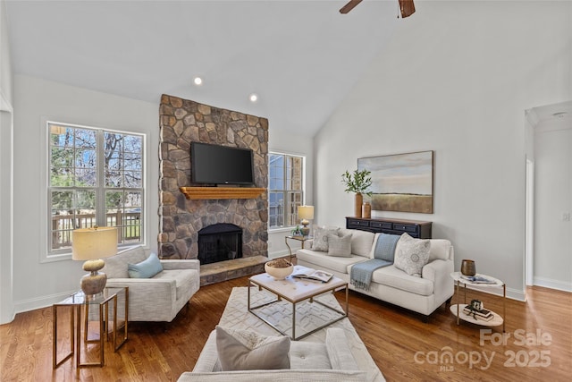 living room featuring high vaulted ceiling, a fireplace, baseboards, and wood finished floors