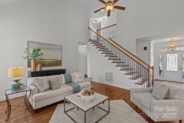 living area with baseboards, visible vents, stairway, wood finished floors, and a high ceiling