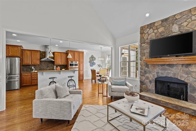 living room featuring high vaulted ceiling, a stone fireplace, wood finished floors, and recessed lighting