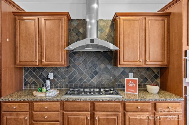 kitchen featuring dark stone counters, stainless steel gas stovetop, wall chimney range hood, and decorative backsplash