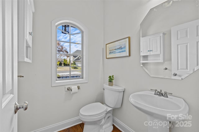 half bathroom with toilet, baseboards, a sink, and wood finished floors