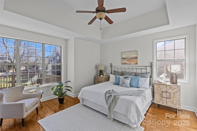 bedroom with multiple windows, a tray ceiling, and wood finished floors