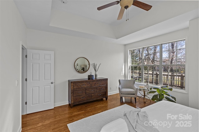 bedroom with a ceiling fan, baseboards, a raised ceiling, and wood finished floors