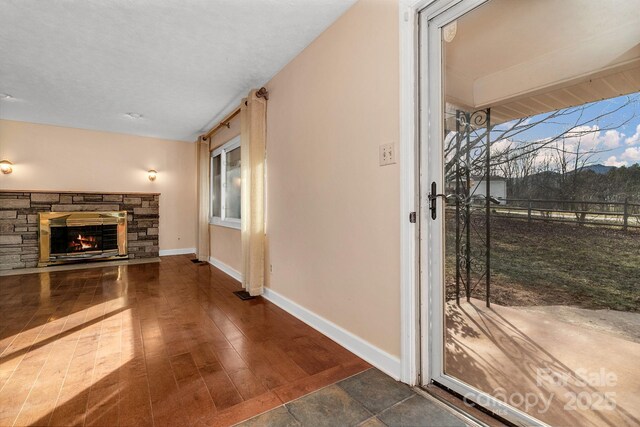 interior space with a wealth of natural light, a stone fireplace, baseboards, and wood finished floors