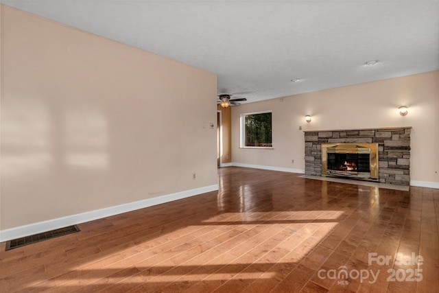 unfurnished living room featuring wood finished floors, visible vents, baseboards, a fireplace, and ceiling fan