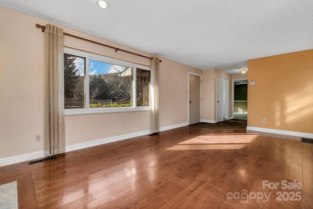 unfurnished room featuring visible vents, baseboards, and hardwood / wood-style floors