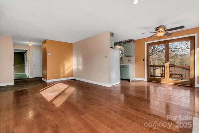 unfurnished living room with dark wood-style floors, ceiling fan, and baseboards