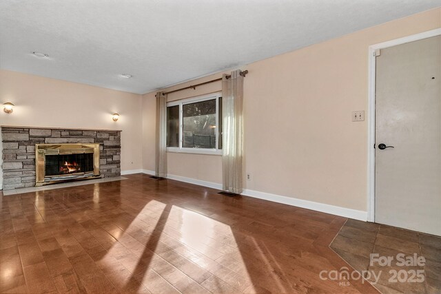 unfurnished living room featuring a stone fireplace, wood finished floors, and baseboards