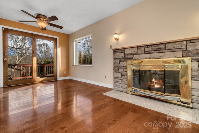 unfurnished living room featuring baseboards, wood-type flooring, a ceiling fan, and a fireplace