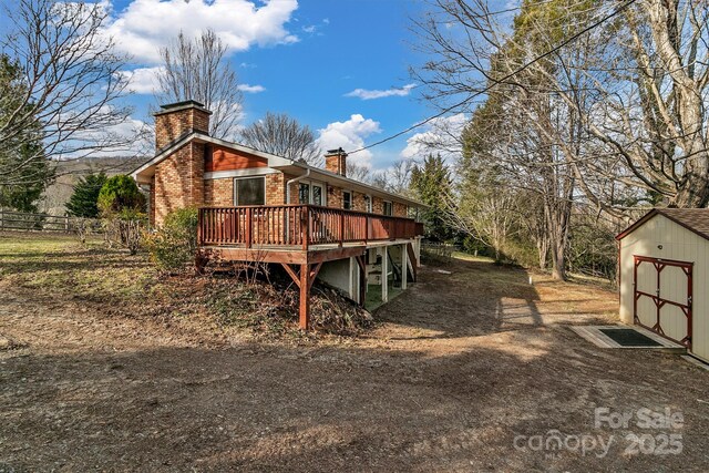 view of side of property with a wooden deck, a chimney, an outdoor structure, a storage shed, and brick siding