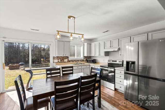 kitchen featuring dark wood finished floors, light countertops, appliances with stainless steel finishes, a sink, and under cabinet range hood