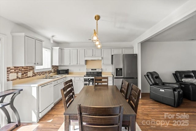 kitchen featuring light wood-style flooring, appliances with stainless steel finishes, hanging light fixtures, light countertops, and backsplash