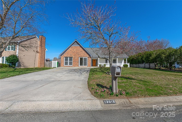 view of front of property featuring brick siding, concrete driveway, a front yard, and fence