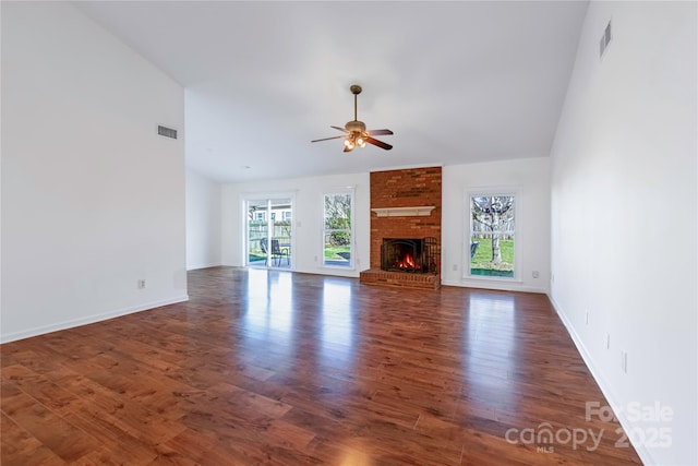 unfurnished living room featuring a brick fireplace, plenty of natural light, wood finished floors, and visible vents