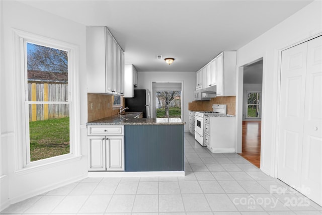 kitchen with backsplash, light tile patterned floors, white cabinets, white appliances, and a sink