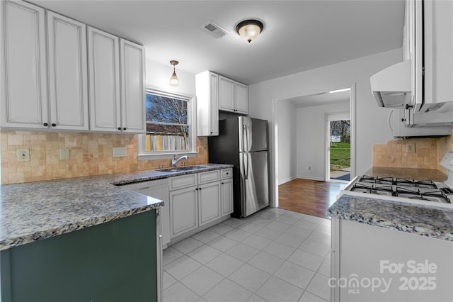 kitchen with visible vents, white gas range, light tile patterned floors, freestanding refrigerator, and a sink