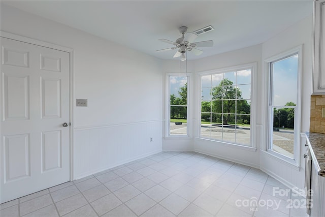 spare room featuring a wainscoted wall, light tile patterned flooring, visible vents, and ceiling fan