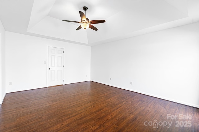 unfurnished room with baseboards, a raised ceiling, dark wood finished floors, and a ceiling fan