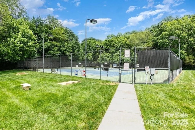 view of tennis court with fence, a lawn, and a gate