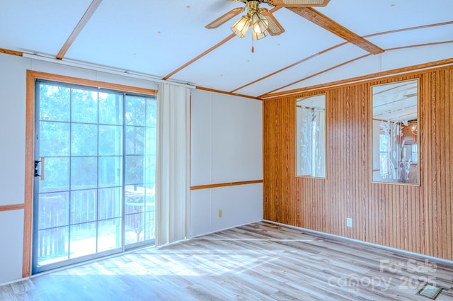 spare room featuring vaulted ceiling with beams, light wood finished floors, a ceiling fan, and wooden walls