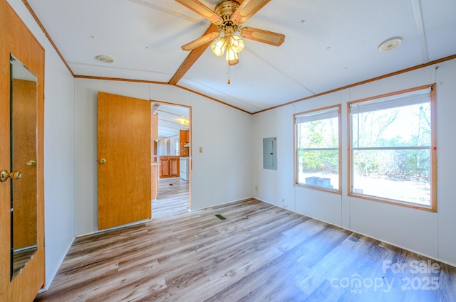 empty room with light wood-type flooring, electric panel, ornamental molding, and vaulted ceiling