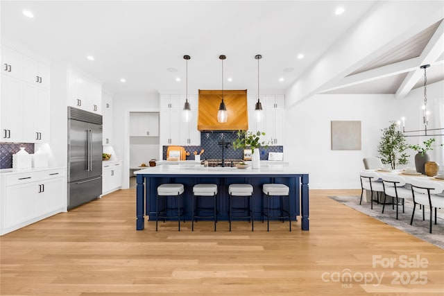 kitchen with light countertops, stainless steel built in fridge, beamed ceiling, and light wood-style flooring