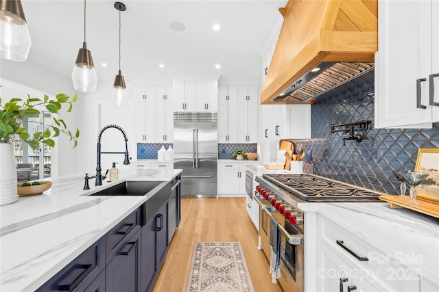 kitchen with built in appliances, premium range hood, a sink, and white cabinetry