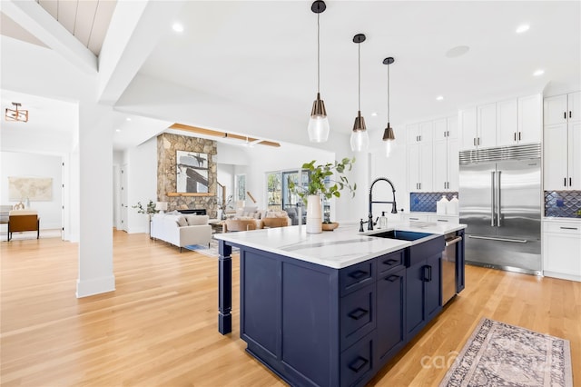 kitchen with appliances with stainless steel finishes, a sink, a stone fireplace, white cabinetry, and backsplash