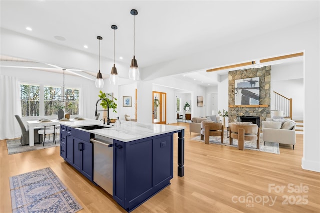 kitchen featuring light wood-style flooring, a fireplace, a sink, stainless steel dishwasher, and blue cabinetry