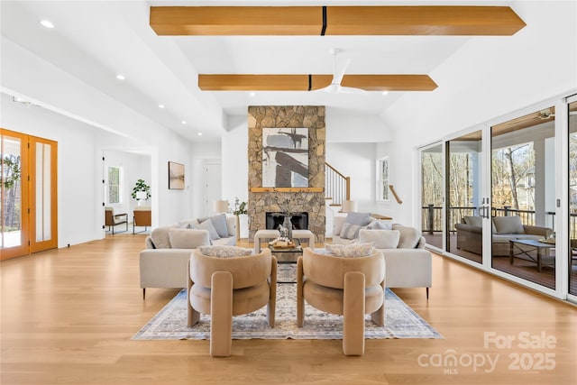 living area featuring a wealth of natural light, a stone fireplace, french doors, and beam ceiling