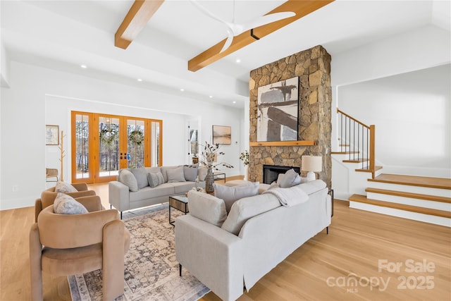 living area featuring beam ceiling, stairway, wood finished floors, and a stone fireplace