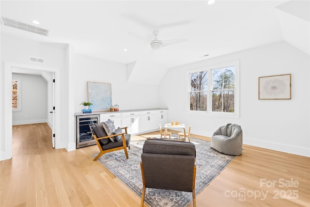 living area with beverage cooler, vaulted ceiling, light wood-type flooring, and visible vents