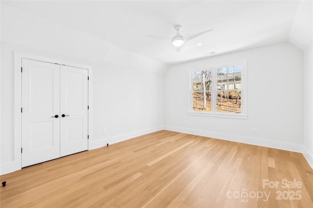 unfurnished bedroom with lofted ceiling, light wood-type flooring, a ceiling fan, and baseboards