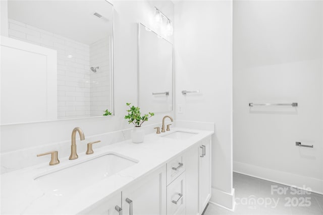 bathroom with a tile shower, double vanity, a sink, and baseboards