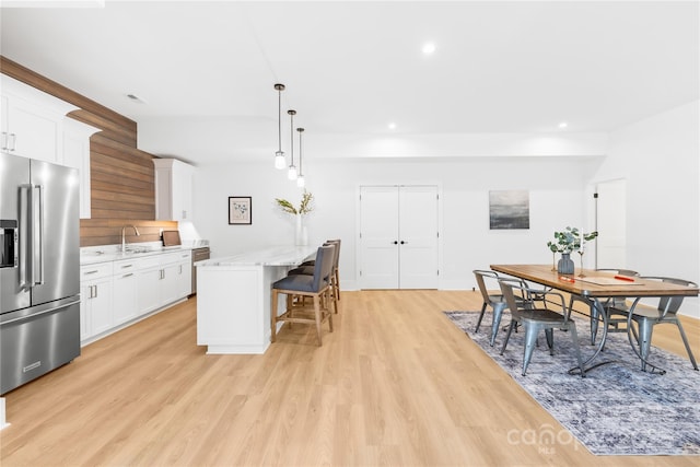 kitchen with a breakfast bar area, stainless steel appliances, a sink, white cabinets, and light wood finished floors