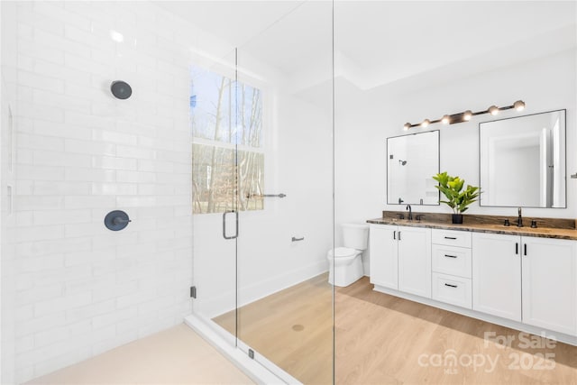 full bath with double vanity, toilet, a stall shower, a sink, and wood finished floors