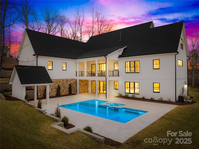 rear view of house featuring a balcony, roof with shingles, a yard, a patio area, and a pool with connected hot tub