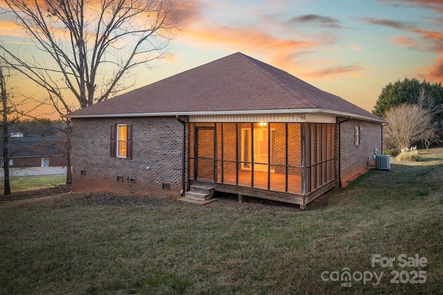 back of property at dusk featuring crawl space, central air condition unit, a shingled roof, and a yard