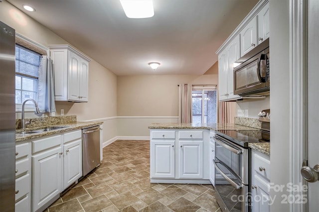 kitchen featuring light stone counters, a peninsula, a sink, white cabinets, and appliances with stainless steel finishes