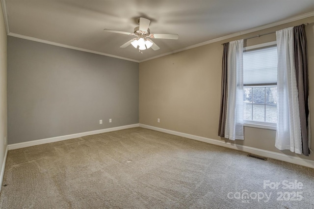 carpeted spare room with ornamental molding, a ceiling fan, visible vents, and baseboards