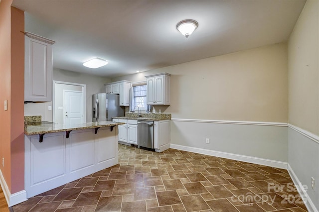 kitchen featuring baseboards, white cabinets, a breakfast bar area, a peninsula, and stainless steel appliances