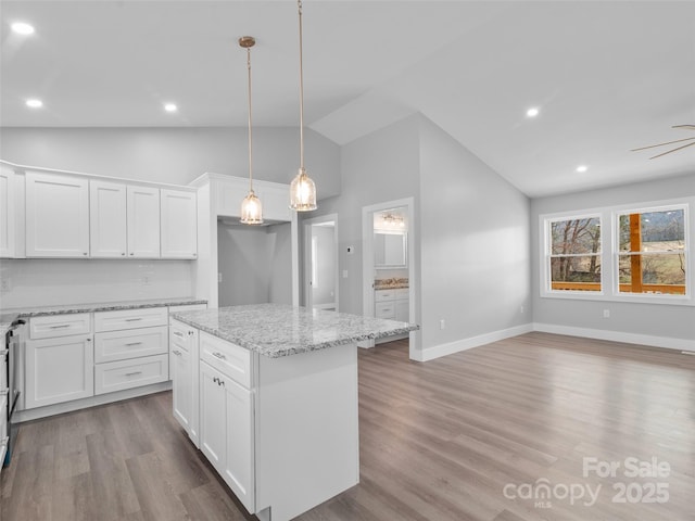 kitchen with a center island, pendant lighting, white cabinets, light stone countertops, and light wood-type flooring