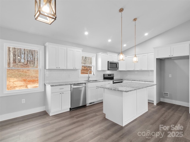 kitchen with appliances with stainless steel finishes, white cabinets, a sink, and decorative light fixtures