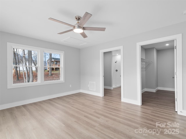 unfurnished bedroom featuring ceiling fan, light wood-style flooring, visible vents, baseboards, and a walk in closet