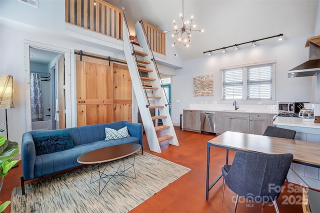 living room with a barn door, a towering ceiling, stairway, rail lighting, and a chandelier