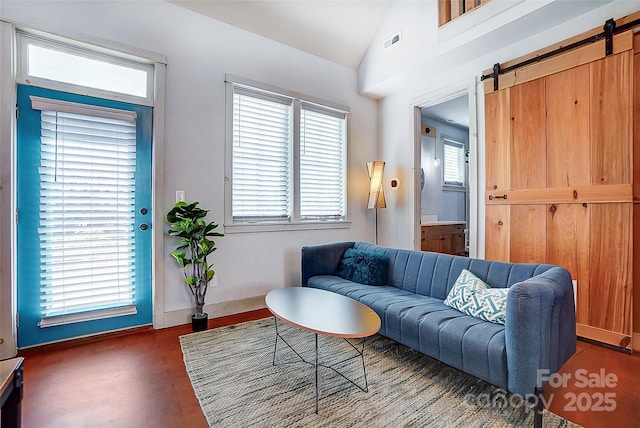 living room with a barn door, baseboards, visible vents, wood finished floors, and vaulted ceiling