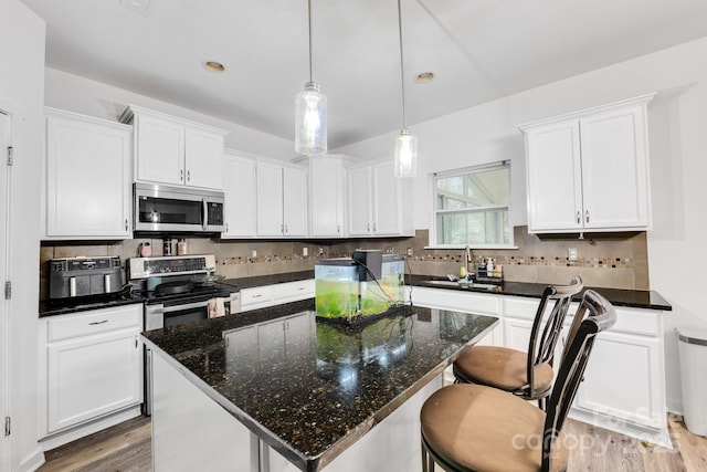 kitchen featuring stainless steel appliances, decorative backsplash, white cabinets, a sink, and wood finished floors