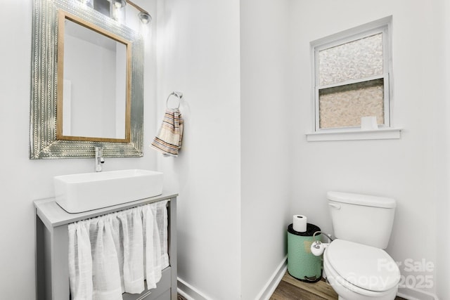 half bathroom with wood finished floors, vanity, toilet, and baseboards