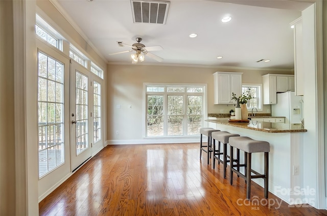 kitchen featuring white refrigerator with ice dispenser, visible vents, crown molding, and wood finished floors